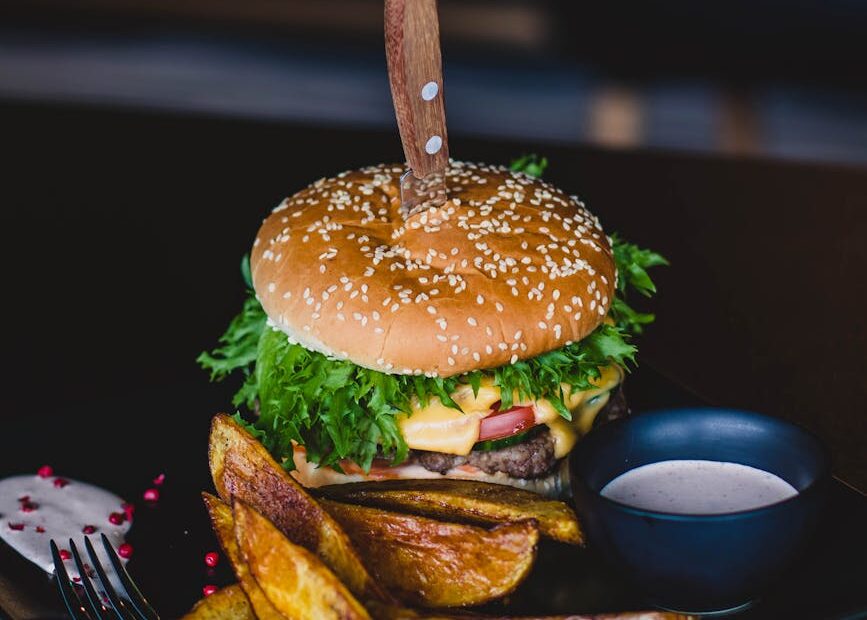 burger with fried fries on black plate with sauce on the side