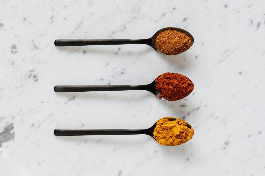 different powdered spices on spoons on marble surface